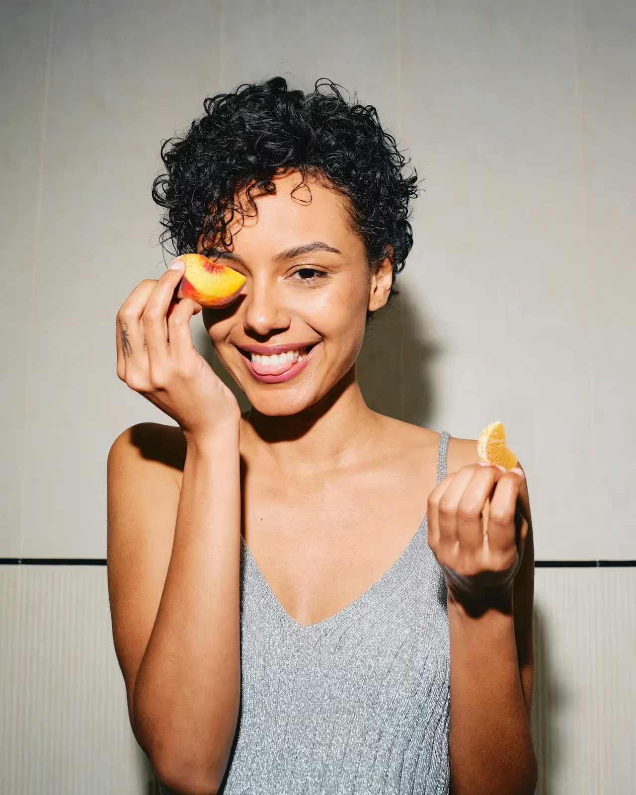 A woman smiling, holding fruit to her eye
